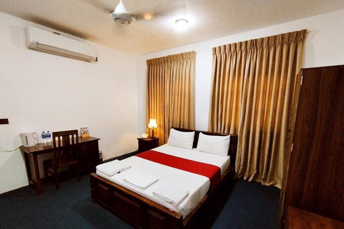 A hotel room with a bed, a desk, a chair, a nightstand, and curtains.