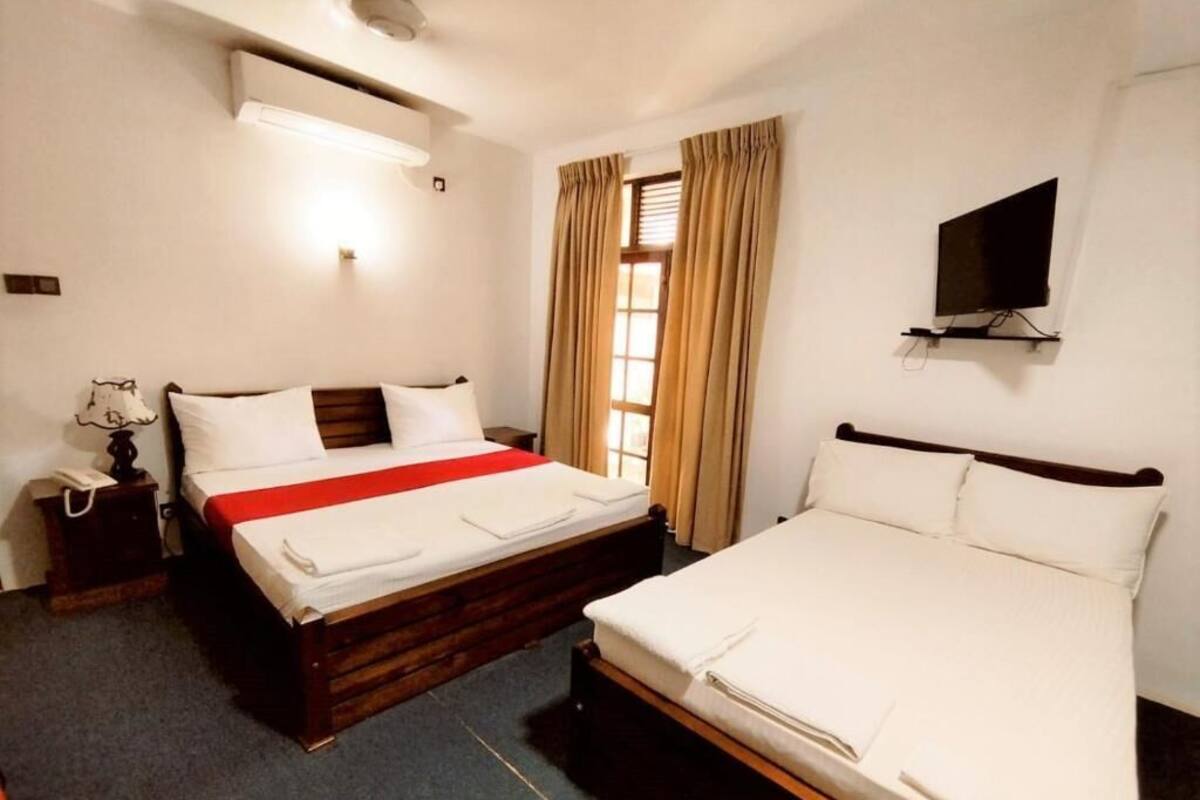 A hotel room with two beds, a TV mounted on the wall, and a window with curtains.