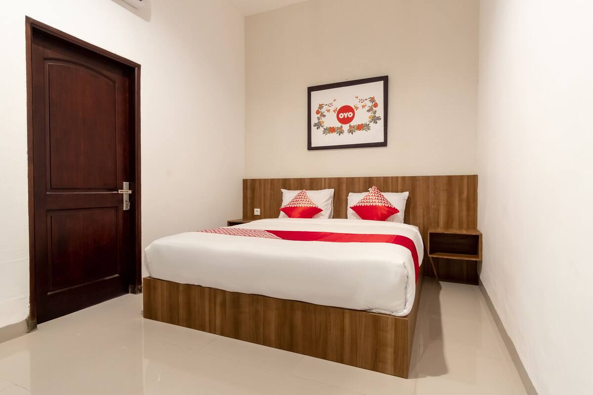 A hotel room with a wooden bed, white bedding, a framed picture on the wall, and a wooden nightstand.
