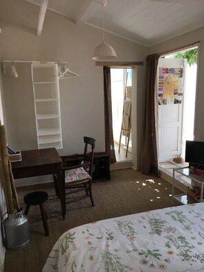 Una habitación con cama, escritorio, silla, lámpara colgante y una puerta que da al exterior.