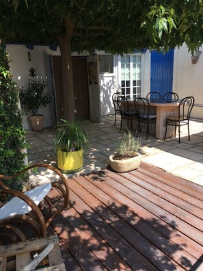 Un patio exterior con una terraza de madera, una mesa con sillas y plantas en macetas.