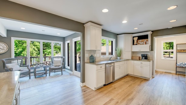 A spacious kitchen with white cabinets, a dishwasher, and a dining area with wicker chairs and a table. - Nights on Normandy (Mooresville)