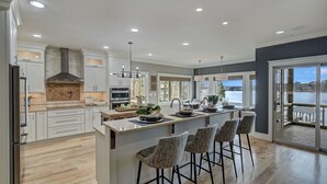 A modern kitchen with a central island, white cabinetry, and a large window overlooking a body of water. - Bridlewood Cove (Mooresville)