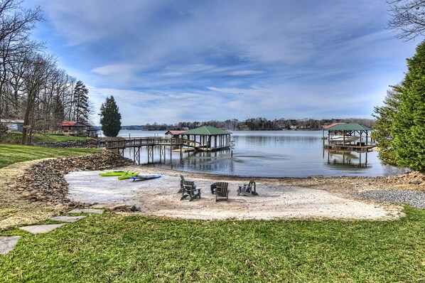 A lakeside property with two docks, a gazebo, and a sandy area with chairs.
