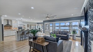 A spacious living area with a large gray sofa, a wooden coffee table, and a view of a lake through large windows. - Bridlewood Cove (Mooresville)
