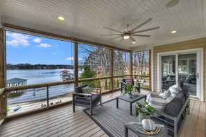 A covered deck with a view of a lake, outdoor furniture, and a ceiling fan.