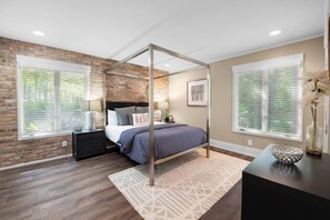 Un dormitorio con una cama con dosel, una pared de ladrillo y ventanas amplias con persianas.
