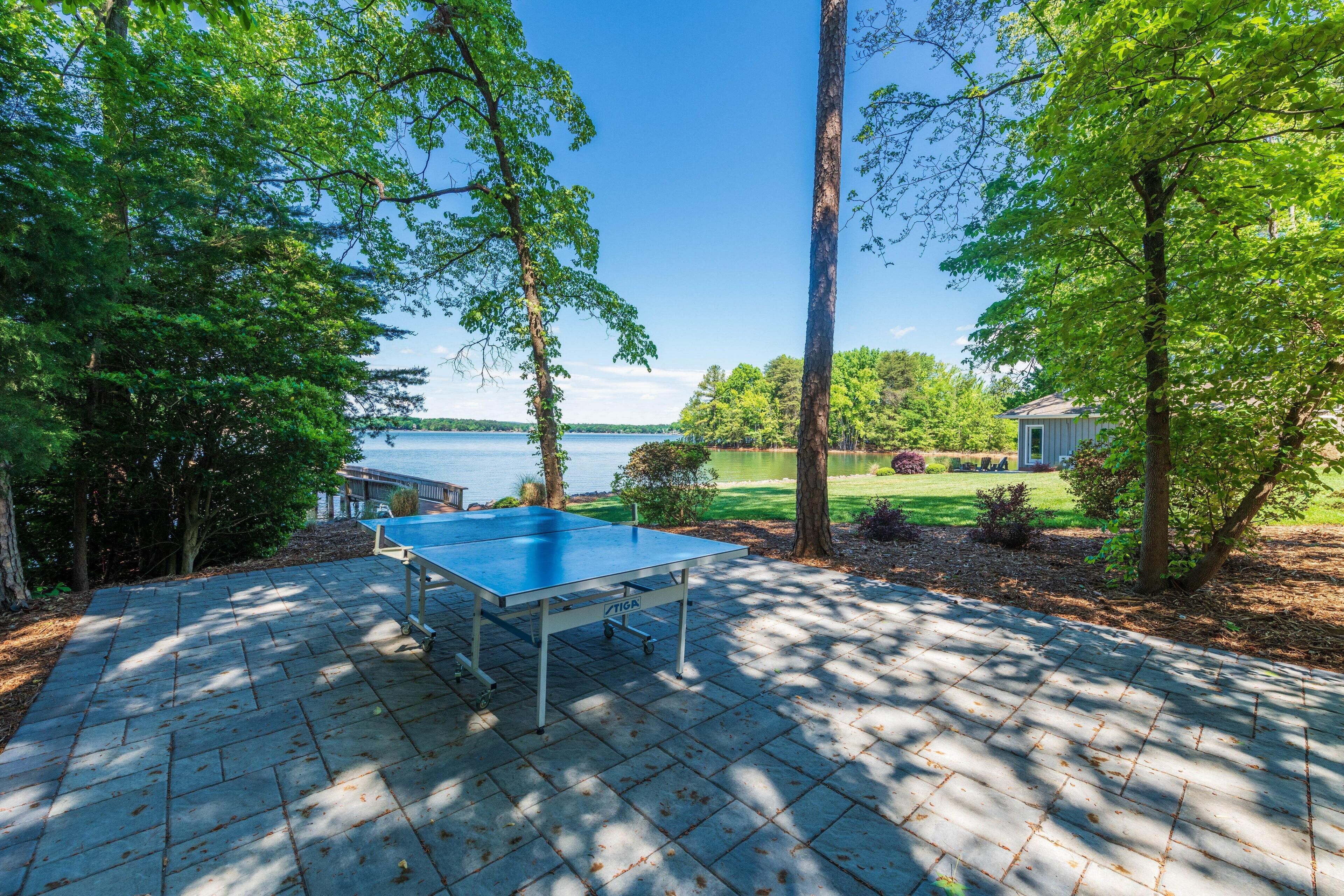 A ping pong table on a paved patio with a lake view.