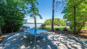 A ping pong table on a paved patio with a lake view.
