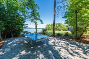 Una mesa de ping pong en un patio empedrado con vista al lago.
