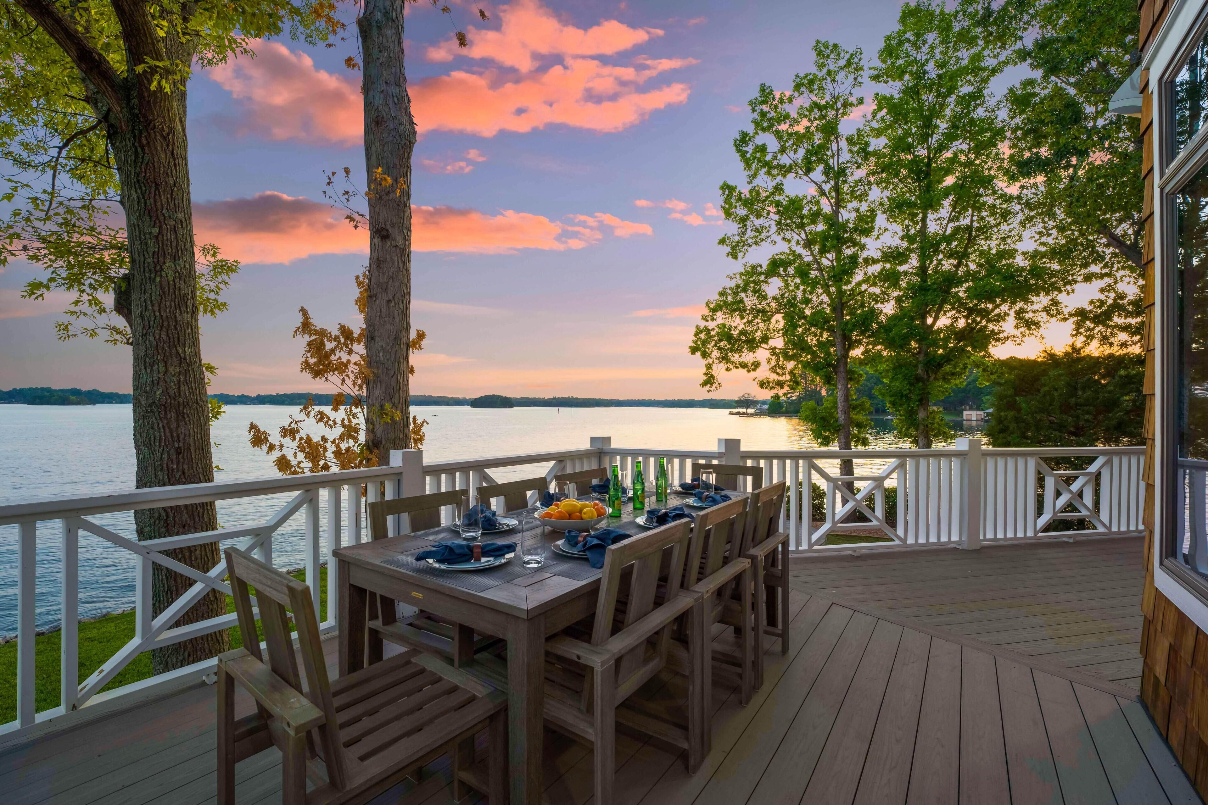 A wooden deck with a table set for dining, overlooking a body of water and trees.