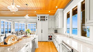 Een moderne keuken met witte kasten, een houten plafond en grote ramen met uitzicht op het water.