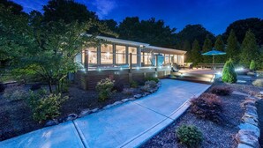 A modern house with a large glass window, a covered patio, and a well-lit garden at night. - Lake Norman Breakaway (Mooresville)