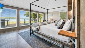 A modern bedroom with a four-poster bed, large windows, and a view of a lake. - Lake Norman Breakaway (Mooresville)