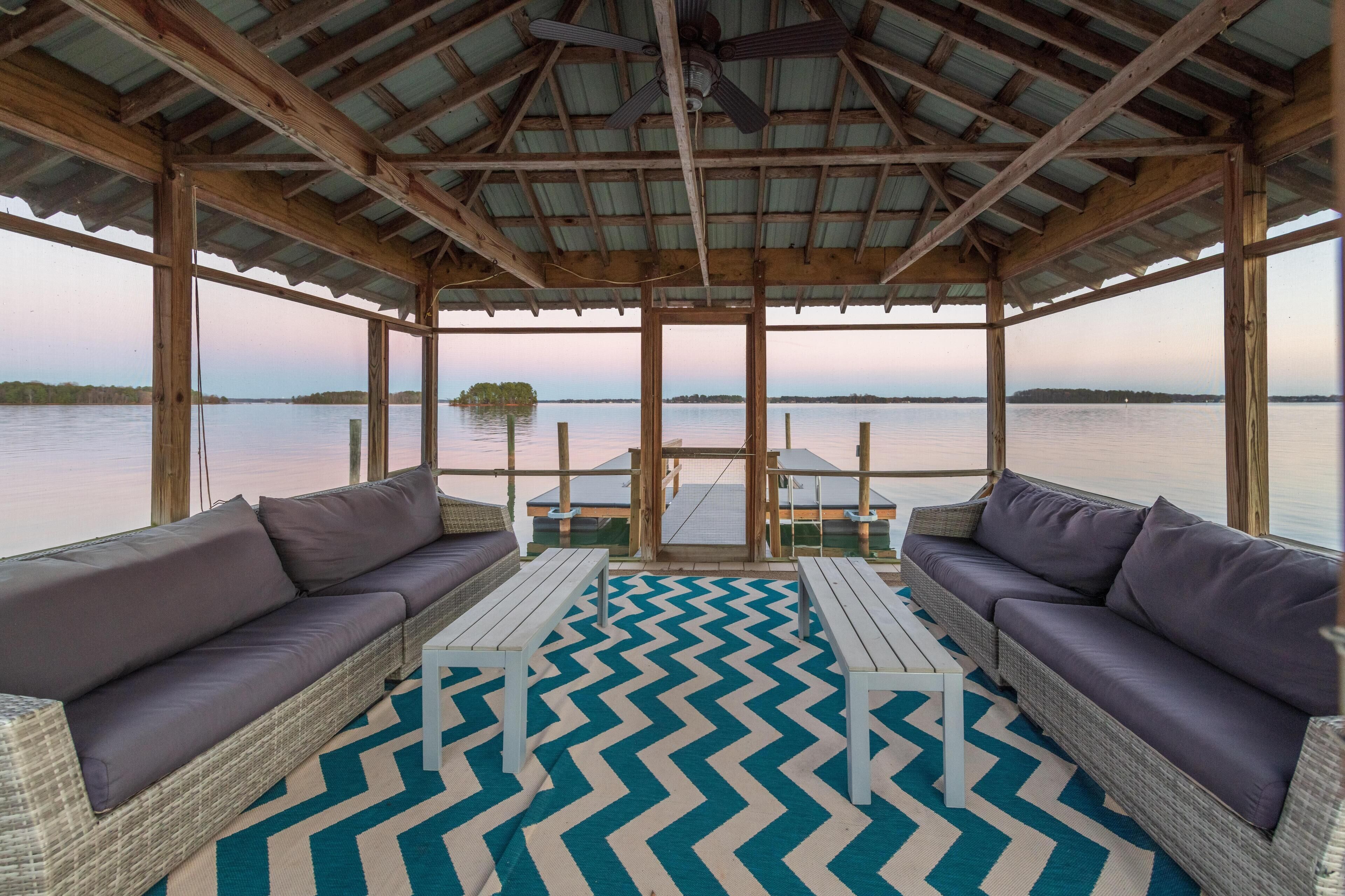 Terraza al aire libre con mobiliario de mimbre y un tapete de diseño en zigzag, con vistas a una masa de agua tranquila.