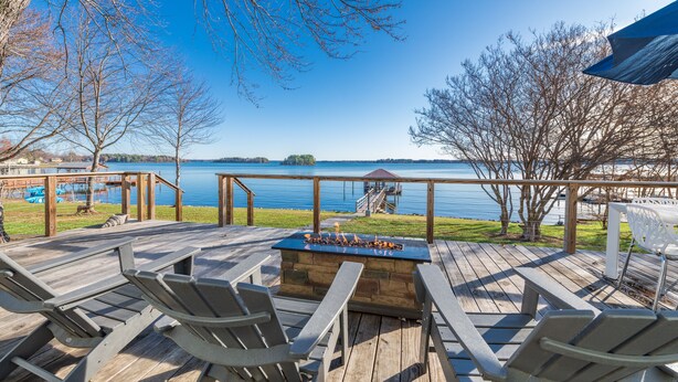 Une terrasse en bois avec des fauteuils Adirondack, un foyer et une vue sur un lac.
