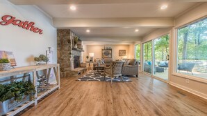 A spacious living room with a stone fireplace, a large window, and a 'Gather' sign on the wall. - No Wake Zone (Mooresville)