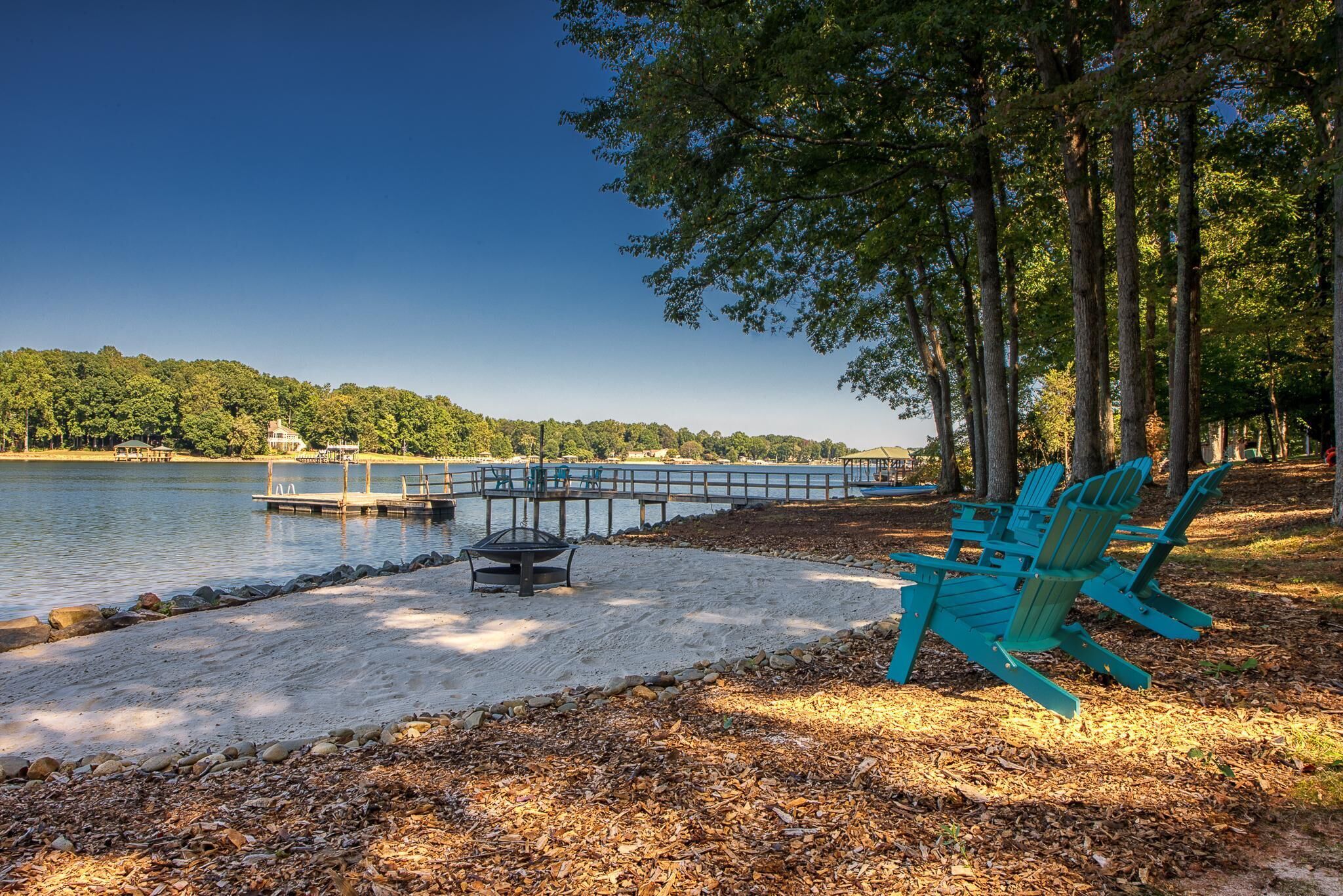 Una terraza junto al lago con sillas Adirondack, un hogar para fogata y un muelle que se adentra en el agua.