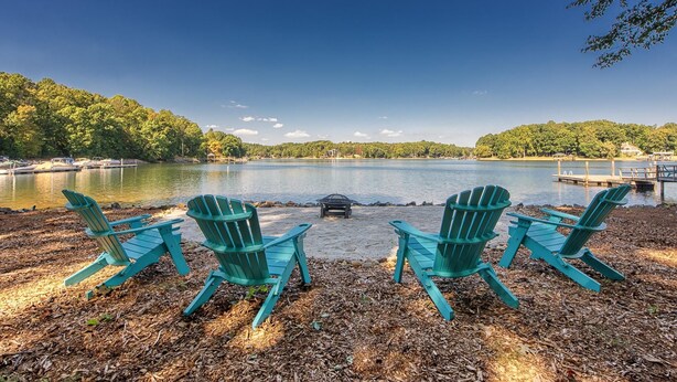 A lakeside view with four green Adirondack chairs facing the water, a dock, and a clear sky. - No Wake Zone (Mooresville)