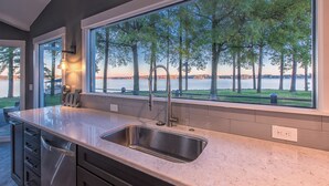 Eine Küche mit einem großen Fenster mit Blick auf einen See und Bäume, einem Edelstahl-Spülbecken und modernen Schränken.