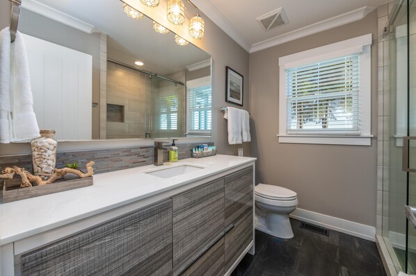 Un baño moderno con un espejo grande, tocador blanco y cabina de ducha de cristal.