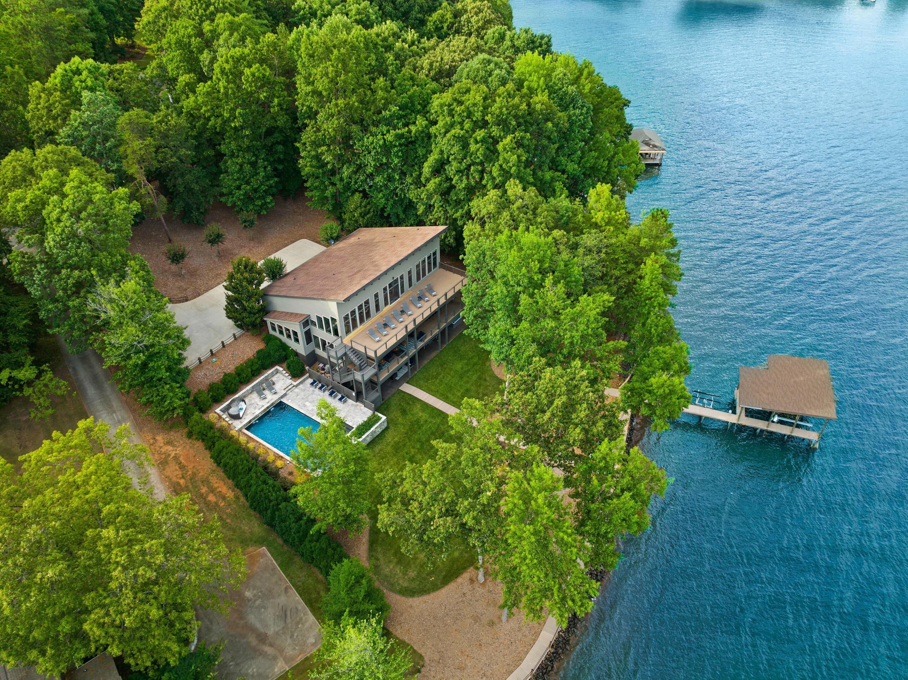 An aerial view of a lakeside property with a large house, a swimming pool, and a dock.