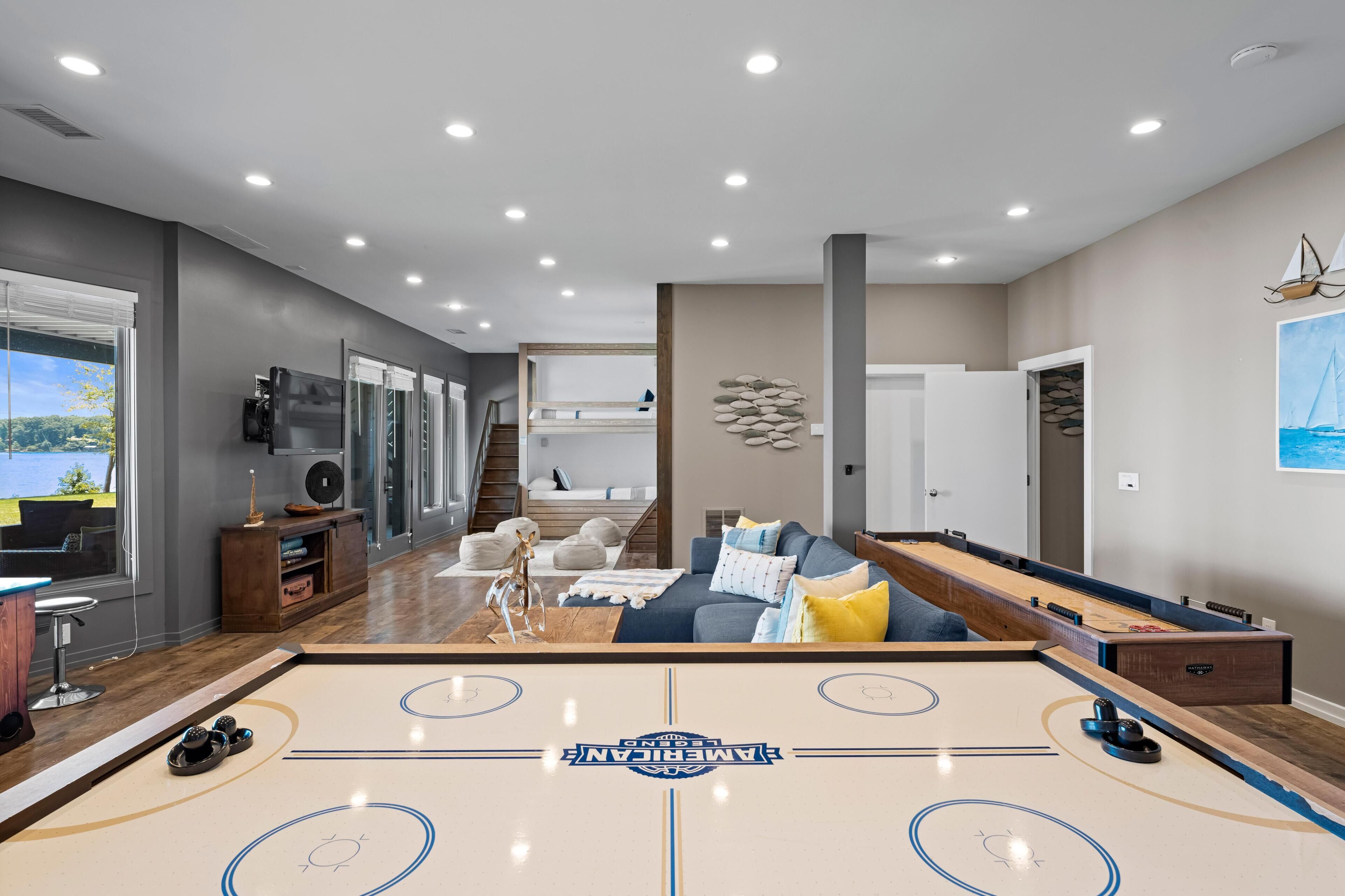 A spacious living area with a shuffleboard table, a sofa, and a view of a balcony.
