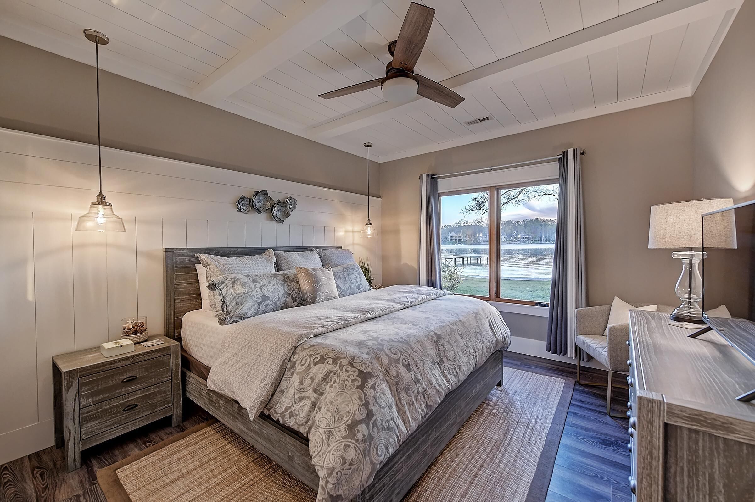 A bedroom with a large bed, a nightstand, a desk, a ceiling fan, and a window with a view.
