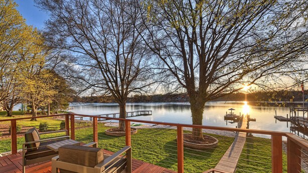 Terraza de madera con mobiliario exterior, vista al lago y un atardecer.
