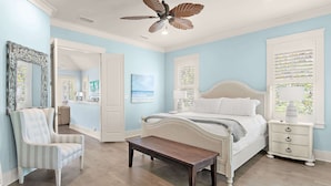A bedroom with a bed, bedside table, nightstand, chair, and a ceiling fan.