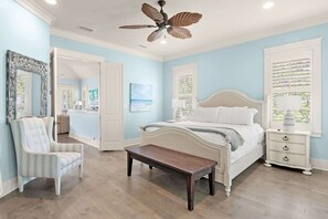 A bedroom with a bed, bedside table, nightstand, chair, and a ceiling fan.