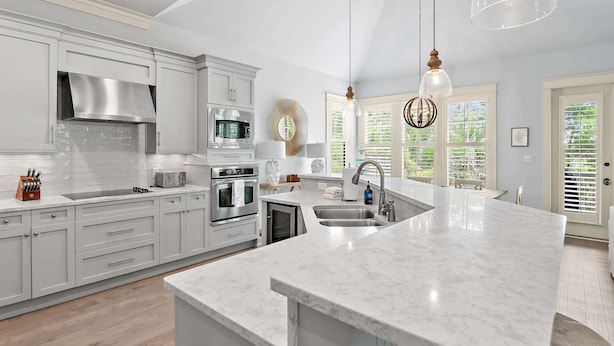 A modern kitchen with white cabinetry, stainless steel appliances, a large island with a sink, and pendant lighting.
