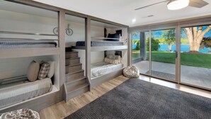 A modern bedroom with bunk beds, a staircase, and a large sliding glass door leading to a balcony with a view of a lake. - Southern Sunrise (Mooresville)