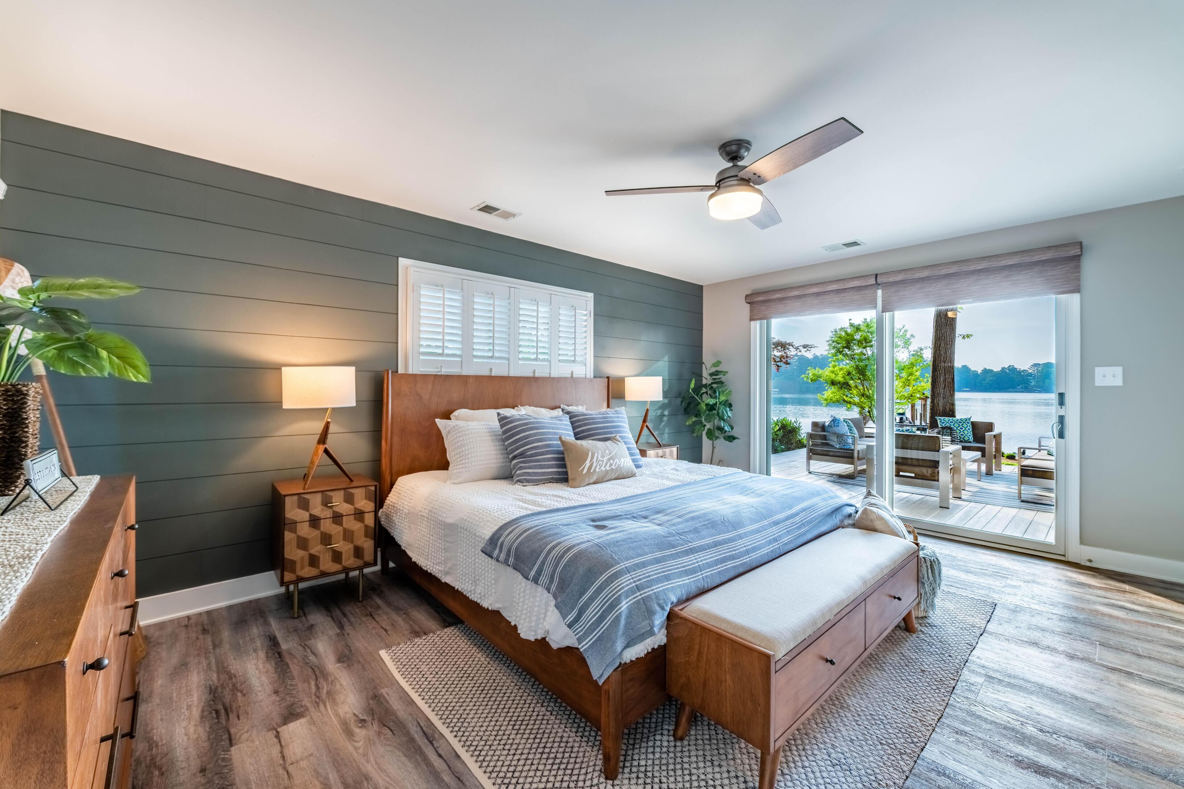 A bedroom with a large bed, a wooden dresser, a nightstand, and a view of the outdoors through a sliding glass door.