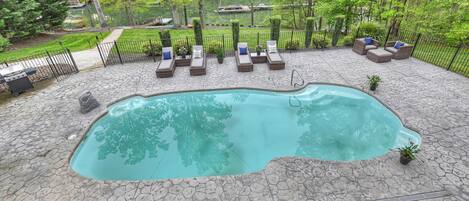 Piscina com deck de pedra, rodeada por espreguiçadeiras e vista para um lago.