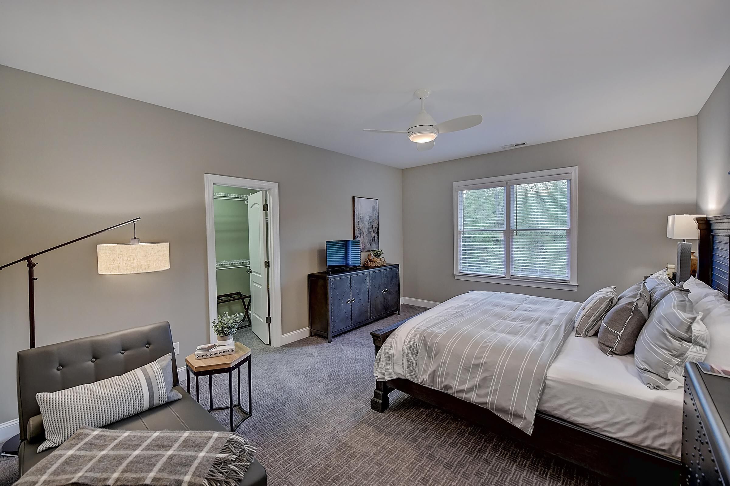 A bedroom with a bed, a desk, a chair, a dresser, and a ceiling fan.
