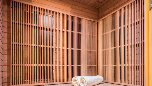 Eine Holzsauna mit einer Sitzbank und einem aufgerollten Handtuch.