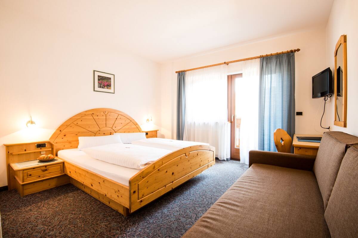 A hotel room with a wooden bed, a desk, a chair, and a TV.