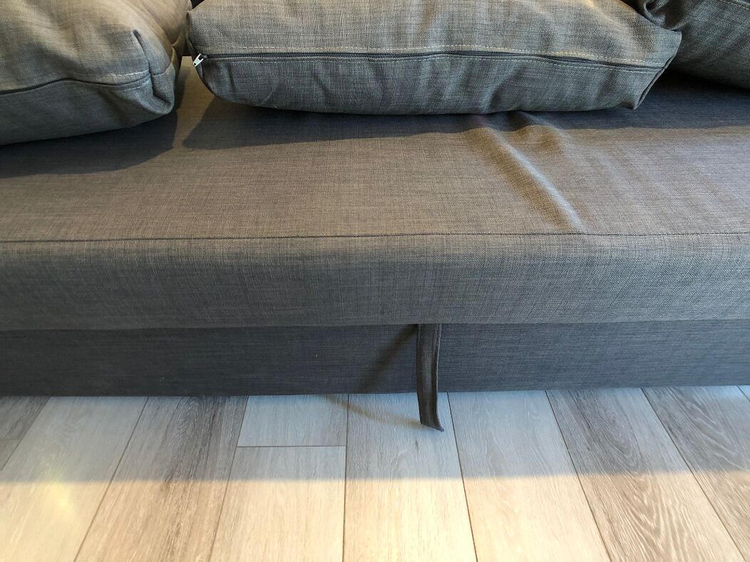 A grey sofa with a zippered pocket and a wooden floor.