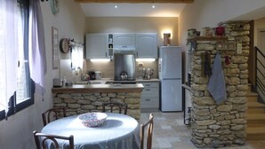 A cozy kitchen with stone walls, wooden beams, and a dining area with a table set for two. - Stone House near Châteauneuf-du-Pape Vineyards (Bédarrides)