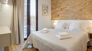 A bedroom with a large bed, a brick wall, a window with curtains, and a framed picture on the wall. - LUCASLAND (Barcelona)
