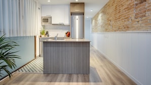 A modern kitchen with a central island, wooden cabinets, and a brick accent wall. - LUCASLAND (Barcelona)