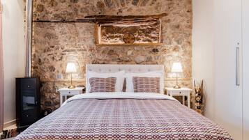 A bedroom with a stone wall, a bed with patterned bedding, two bedside tables with lamps, and a clock on the wall.