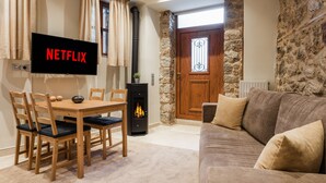 Una sala de estar acogedora con una televisión mostrando "NETFLIX", una chimenea, paredes de piedra, una puerta de madera y un sofá.