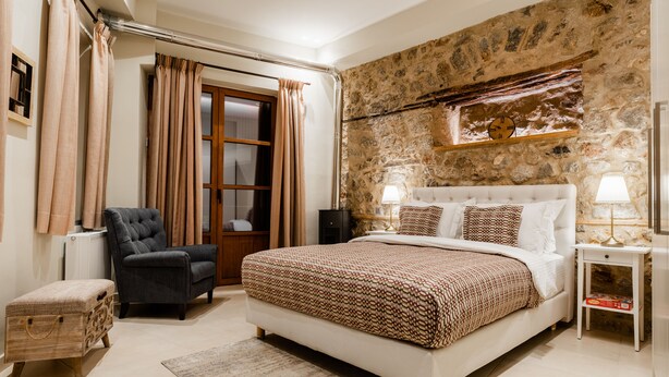 Un dormitorio con una cama grande, una silla, una mesita de noche y una pared de piedra.