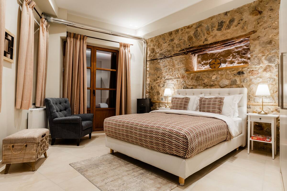 Une chambre avec un grand lit, une chaise, une table de chevet et un mur en pierre.