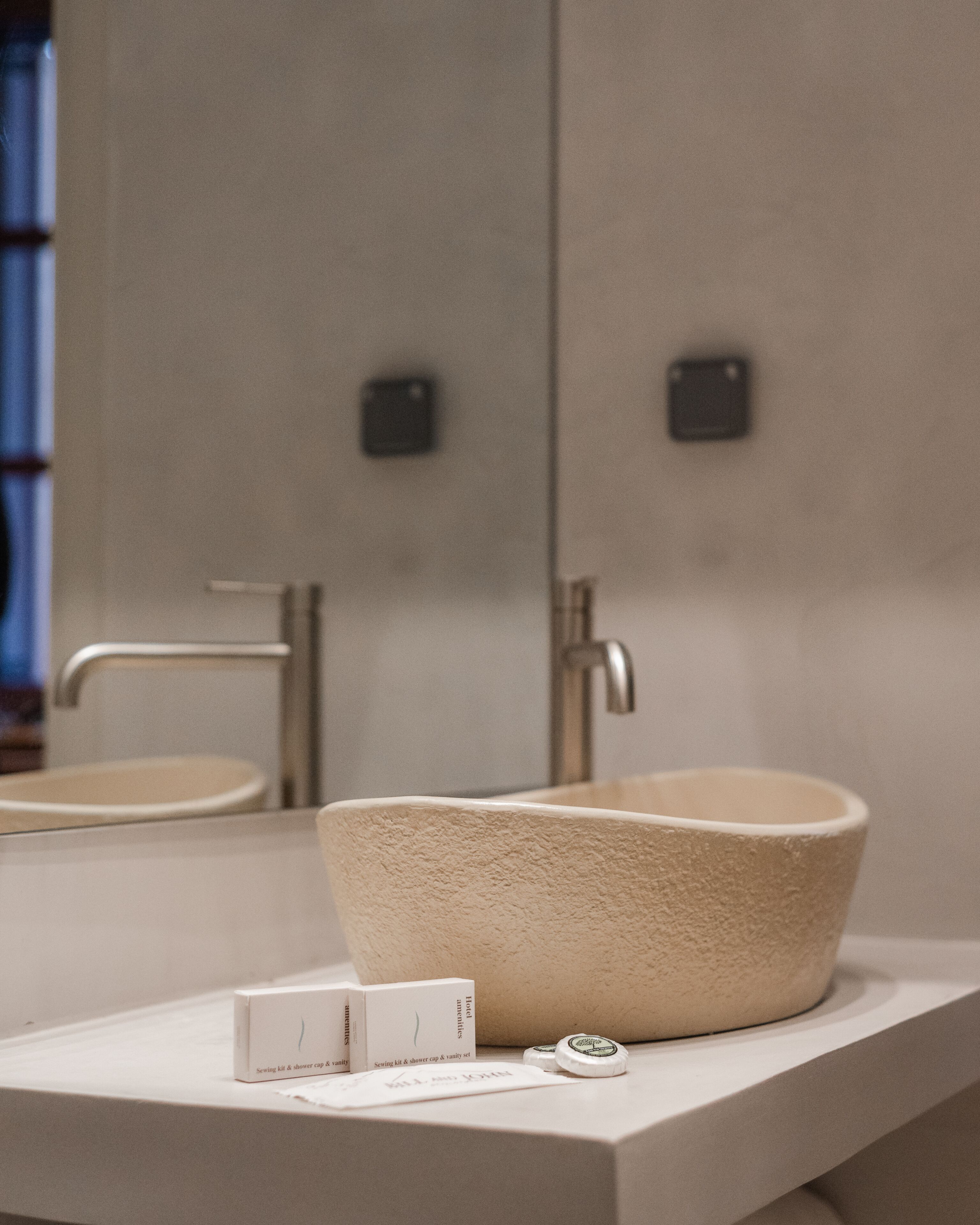 A modern bathroom with a large beige sink and two faucets. There is a small mirror above the sink and a white countertop.