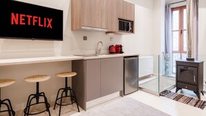 Una cocina moderna con microondas integrado, cafetera y lavavajillas. Hay tres taburetes debajo de la encimera, y un televisor de pantalla plana en la pared mostrando el logotipo de Netflix.