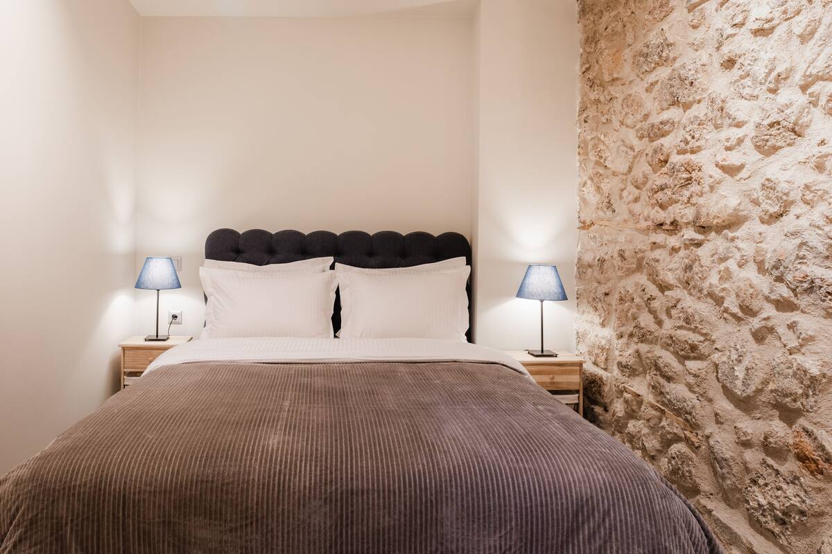 Une chambre à coucher avec un lit, deux tables de chevet et un mur en pierre.