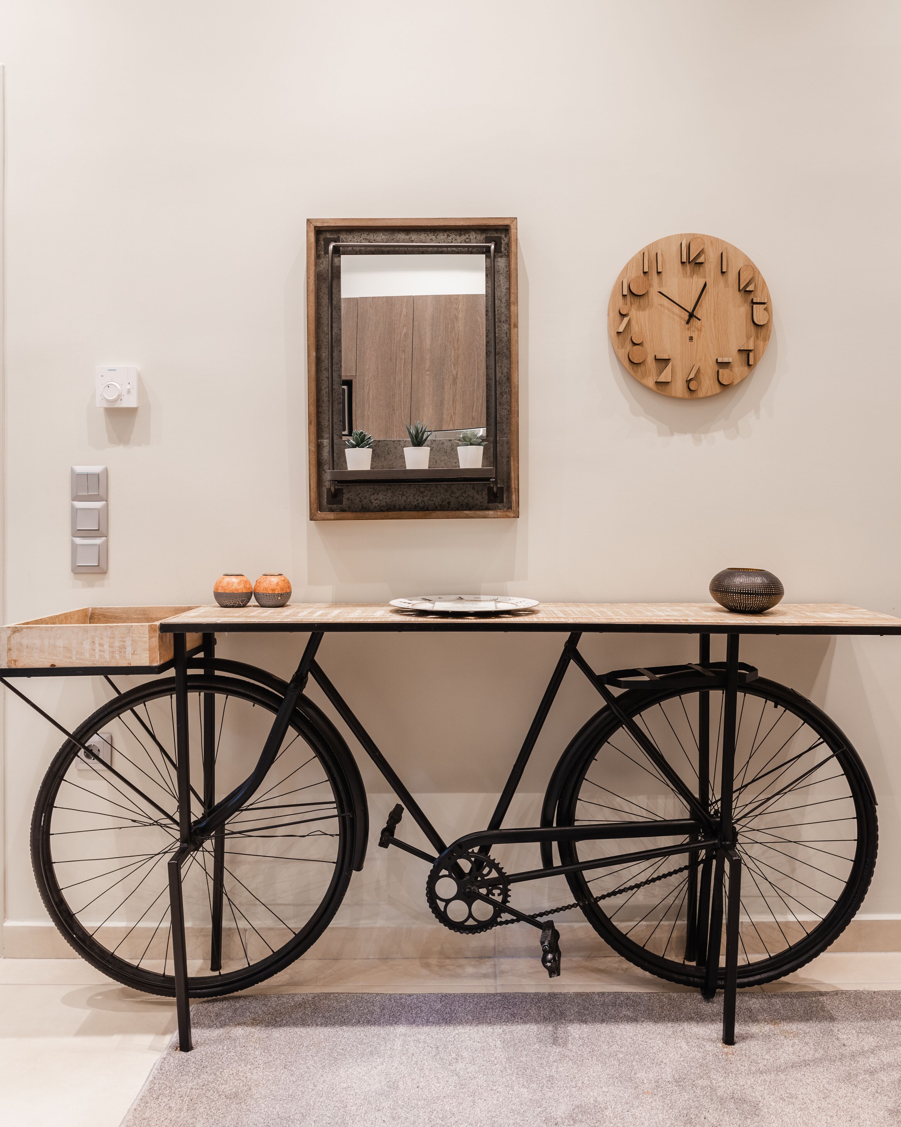 Una habitación con una bicicleta convertida en mesa, un reloj de madera y un espejo en la pared.